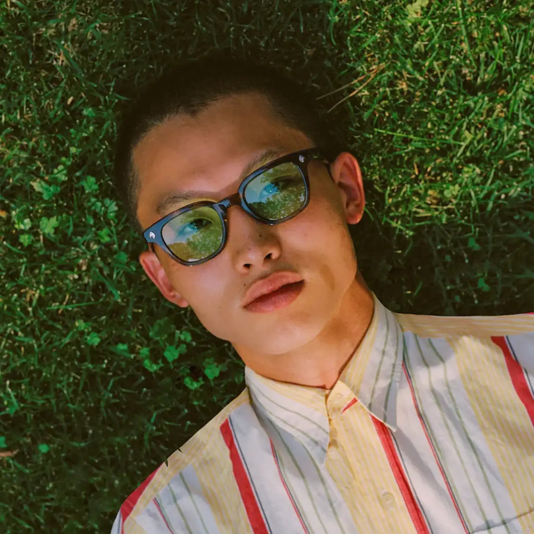 Model laying on grass with GLCO Naples glasses with custom tinted eyeglass lenses with medium green tint