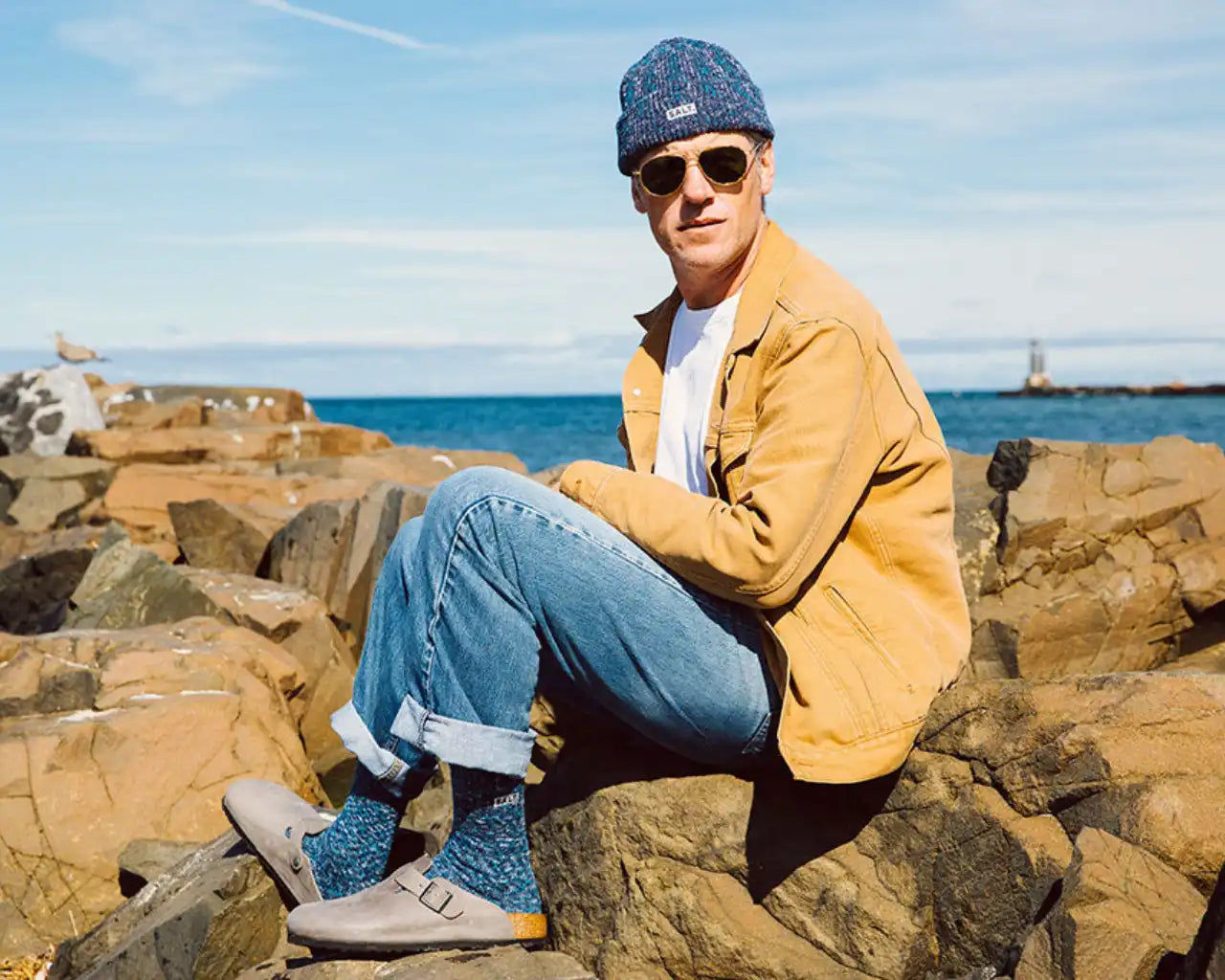 Man sitting on rocks at bay wearing SALT prescription luxury sunglasses