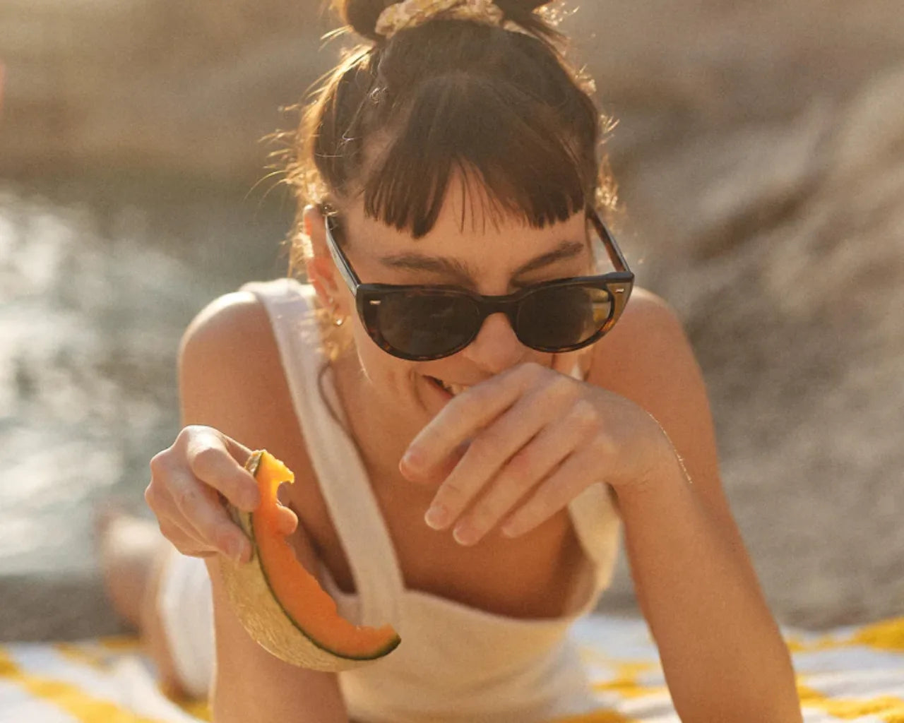 Woman on beach wearing SALT sunglasses eating fruit