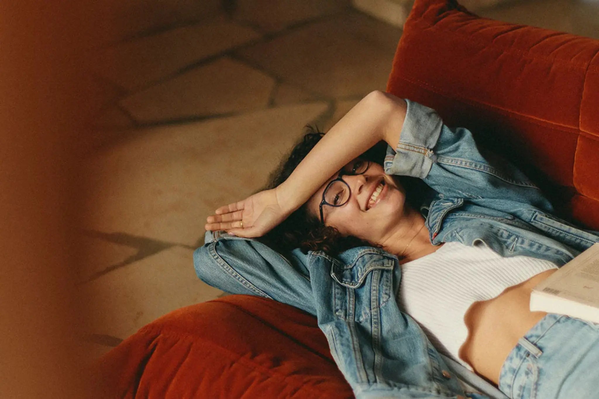 Person lying on a red couch wearing a denim jacket and white shirt, with a warm and cozy atmosphere. Photo credit: SALT.