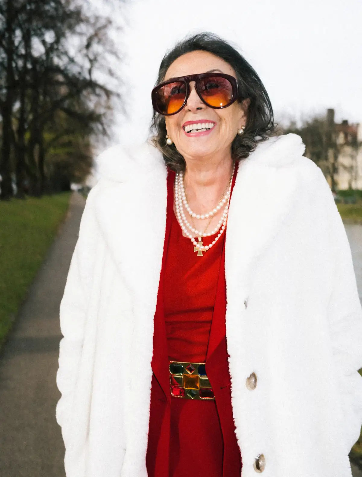 Woman wearing a red dress with a white fur coat and Andy Wolf sunglasses outdoors.