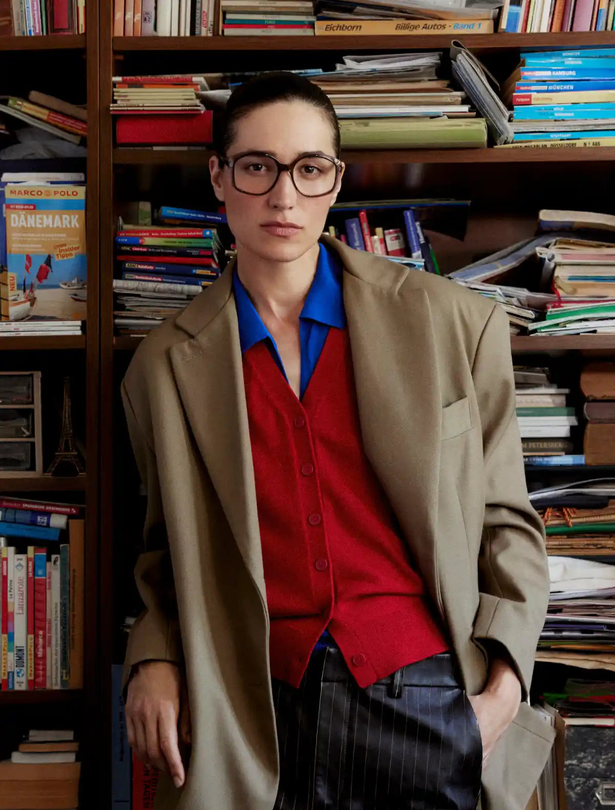 Model standing in front of cluttered bookcase wearing Andy Wolf eyeglasses  and brown coat. Image credit: Andy Wolf