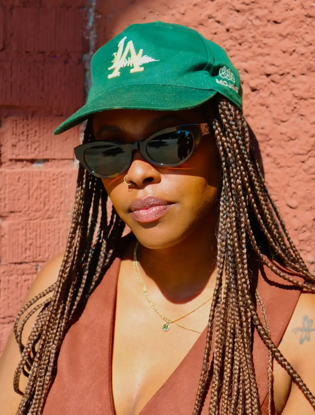 Person wearing a green cap and Article One sunglasses with a red brick wall background. Image credit: Article One