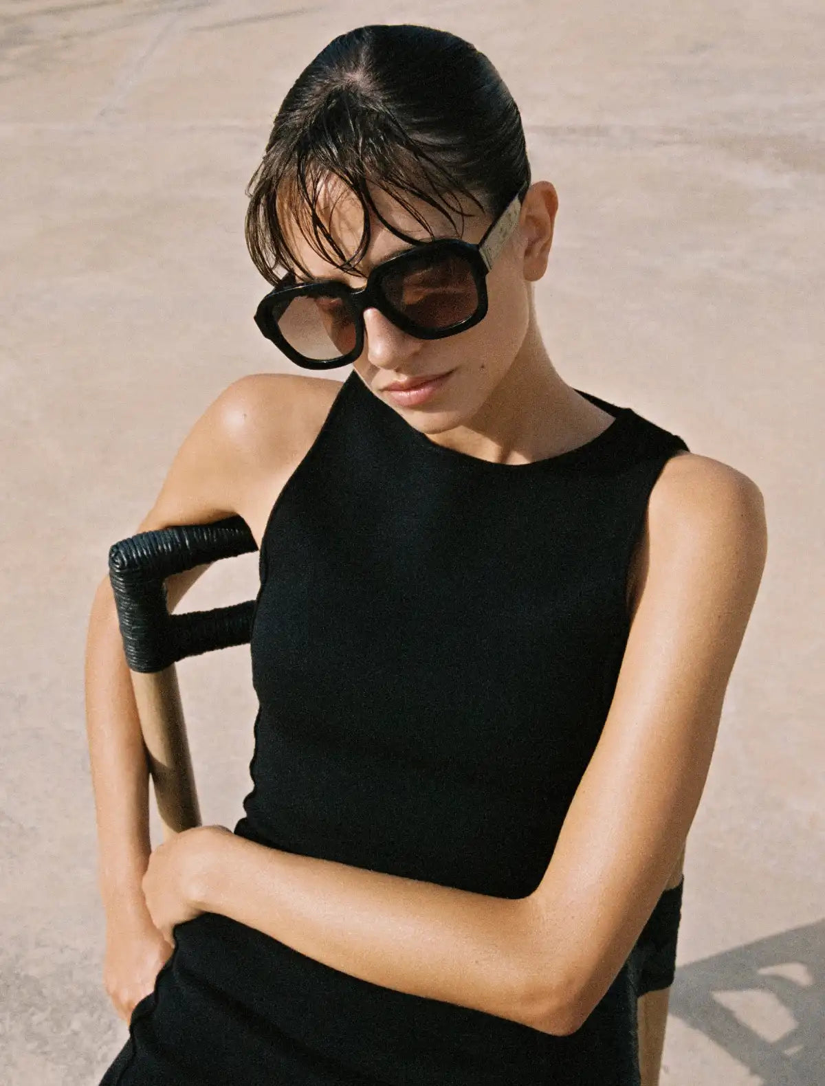 Woman wearing a black sleeveless top and Andy Wolf sunglasses against a beige background