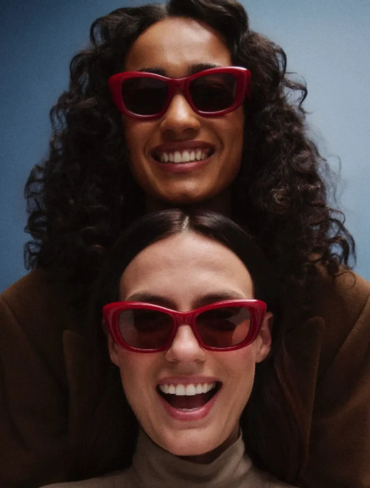 Two people wearing red GLCO sunglasses with a blue background