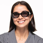 A smiling woman with dark hair wearing black cat-eye sunglasses and a black-and-white striped blazer, photographed against a plain white background. Image credit: SALT